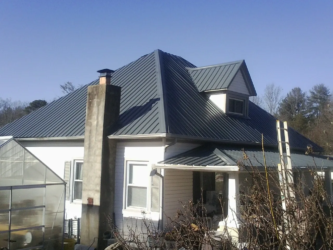 Dark blue standing seam metal roof on a white farmhouse with dormer — Slate & Tile Roof Repair by Roofing Brothers in Rhinelander