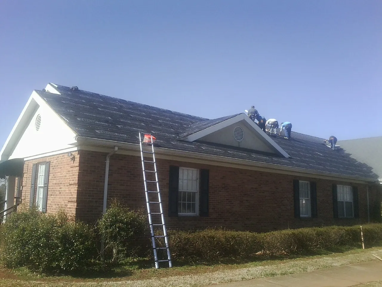 Crew tearing shingles off a brick ranch roof with a ladder set — Metal Roof Repair work by our crew in Rhinelander