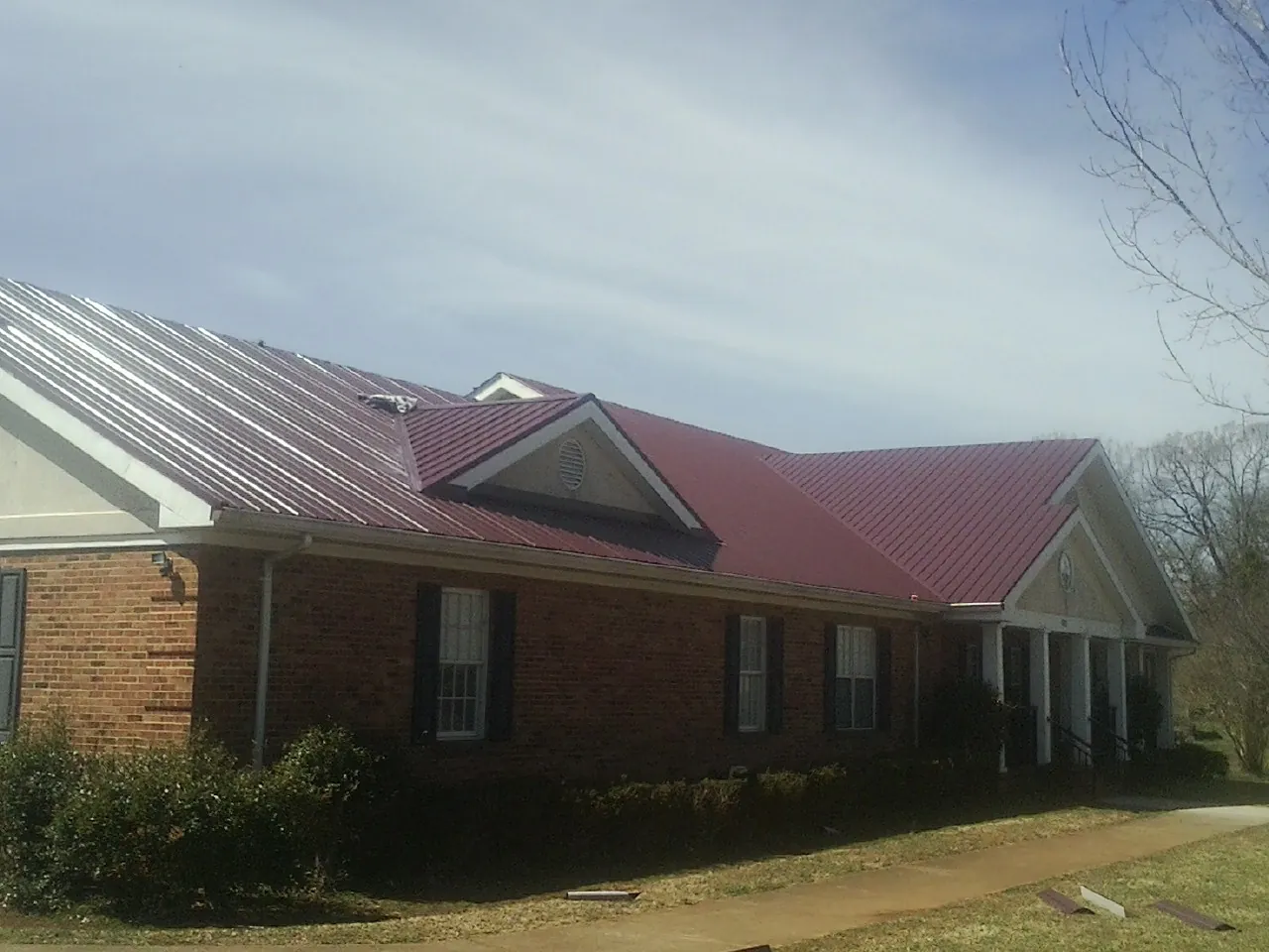Red metal roof with gabled entries on a long brick building, from a Hail Damage Roof Repair job in Rhinelander