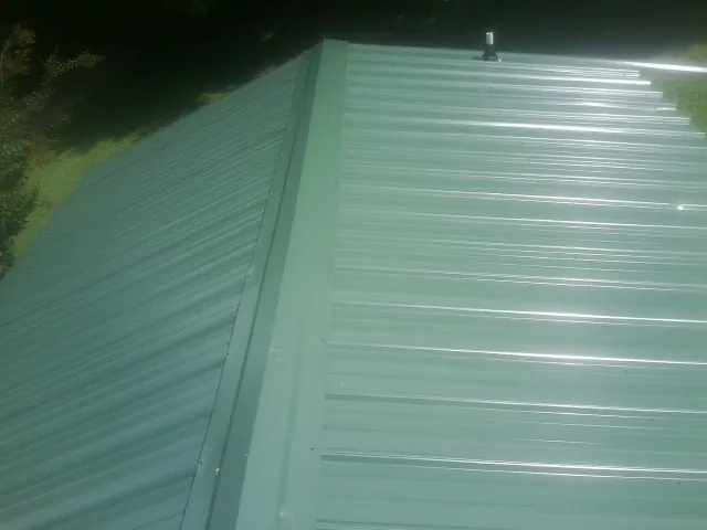 New green metal panels meeting at the ridge of a roof — Flat Roof Repair work by our crew in Rhinelander