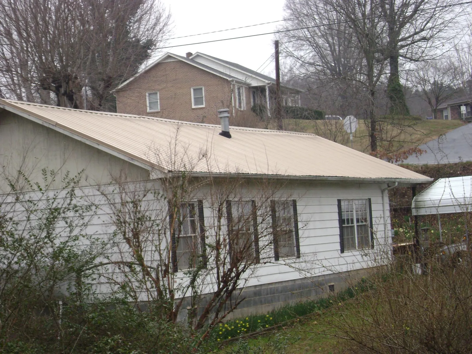 Tan metal roof on a white sided house set into a hillside — Commercial Roofing by Roofing Brothers in Rhinelander