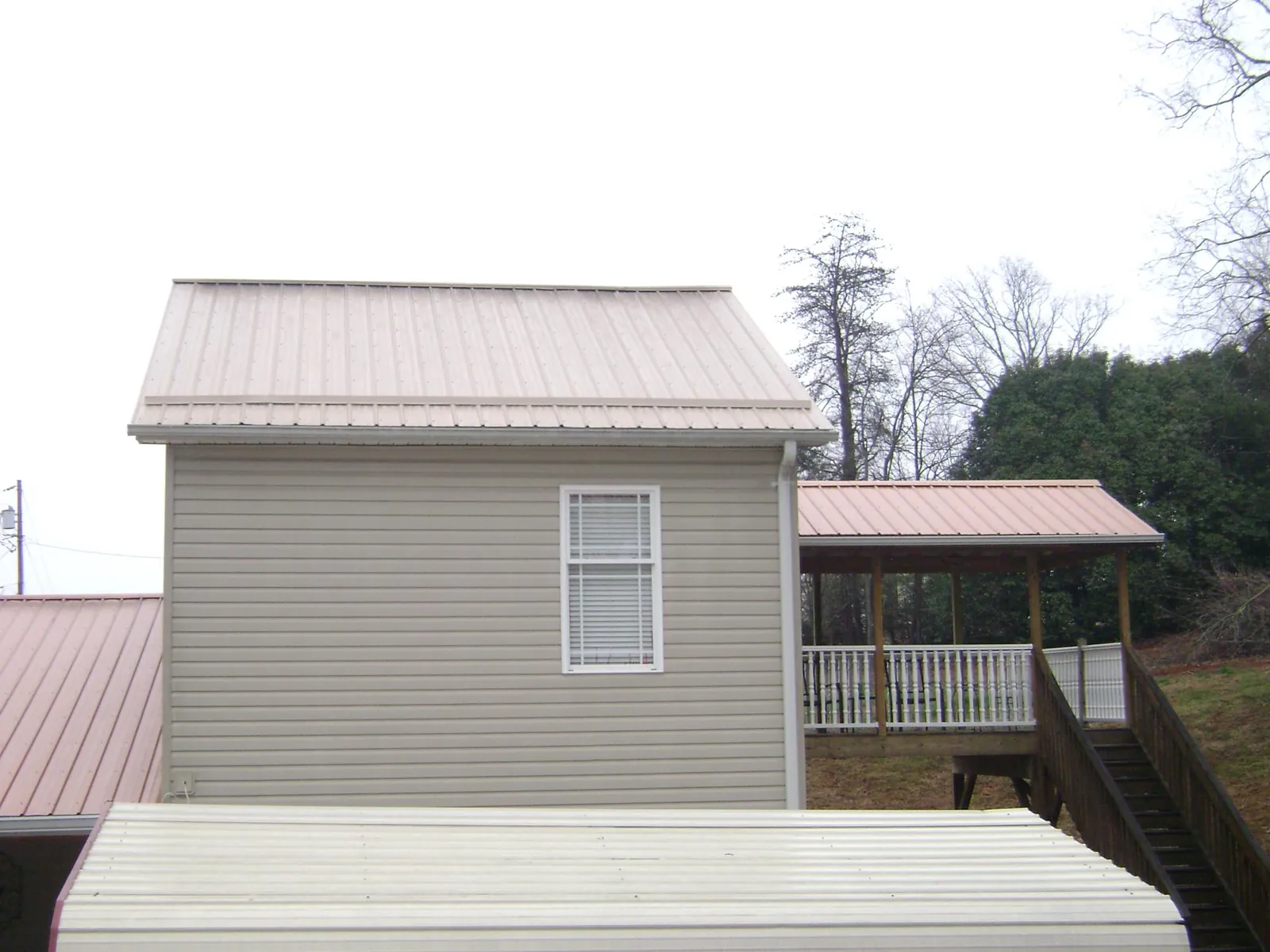 Tan metal roofs on a two story addition and attached porch, from a Roof Replacement job in Rhinelander